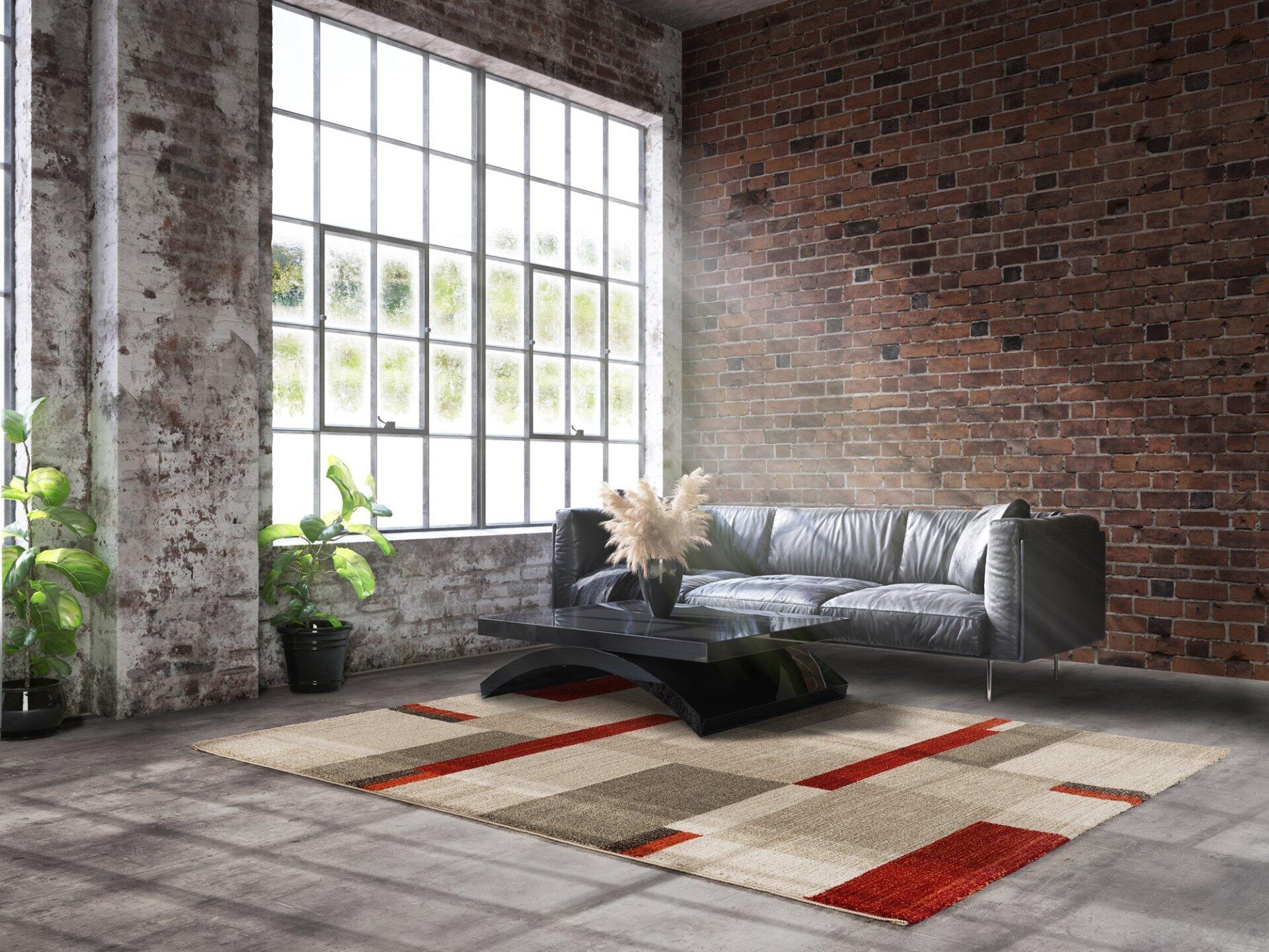 Maschinenwebteppich Salda mit geometrischem Muster aus Rot, Grau und Beige in einem stilvollen Wohnzimmer auf Betonboden.