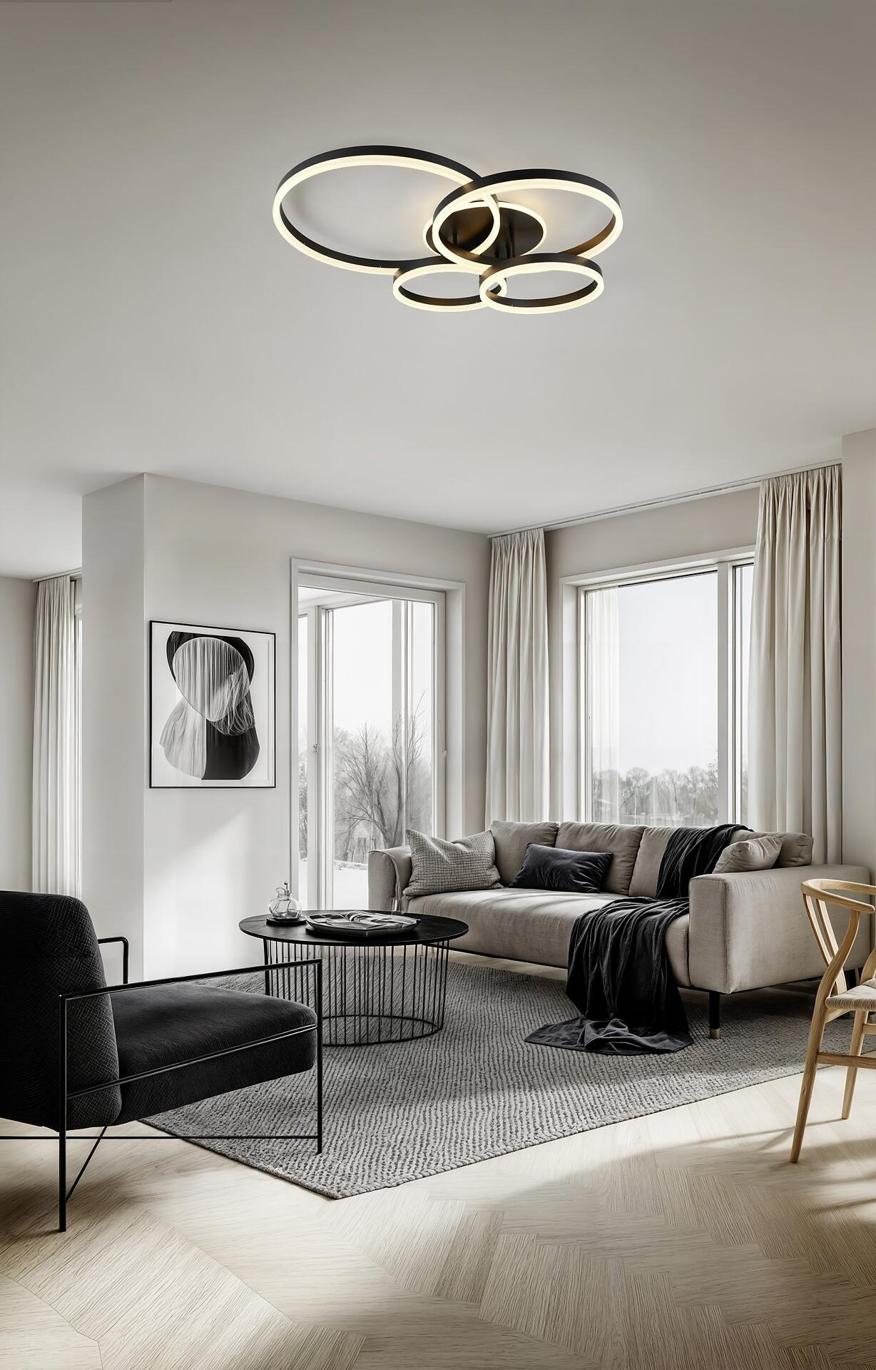 Deckenleuchte Drake mit drei ineinander verschlungenen Metallringen, die warmes, indirektes Licht abgibt und in eine moderne Wohnzimmer-Szene integriert ist.