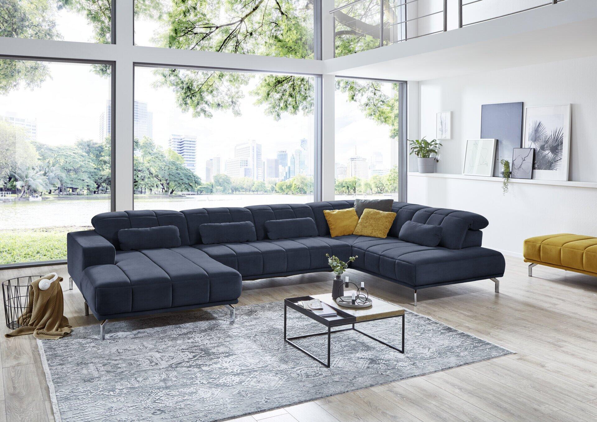 Dunkelblaue Eckcouch Klagenfurt mit modularer Bauweise, linksseitiger Chaiselongue und Kopfteilverstellung auf silbernen Metallfüßen, fotografiert aus erhöhter Perspektive in einem modernen Wohnzimmer.