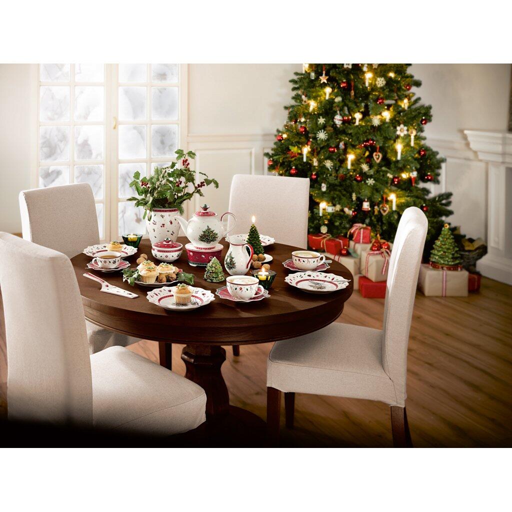 Festlich gedeckter runder Holztisch mit Milchkaffee-Obertassen der Kollektion Toy's Delight von Villeroy & Boch, umgeben von Stühlen und Dekorationen in einer weihnachtlich geschmückten Umgebung.