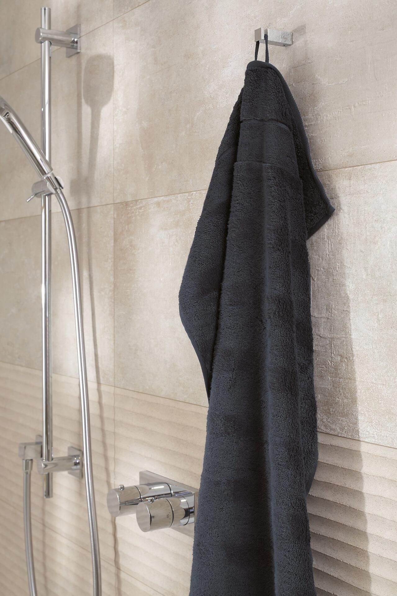 Flauschiges Gästetuch Noblesse² in Schwarz, aufgehängt an einem silberfarbenen Wandhaken in einem Badezimmer.