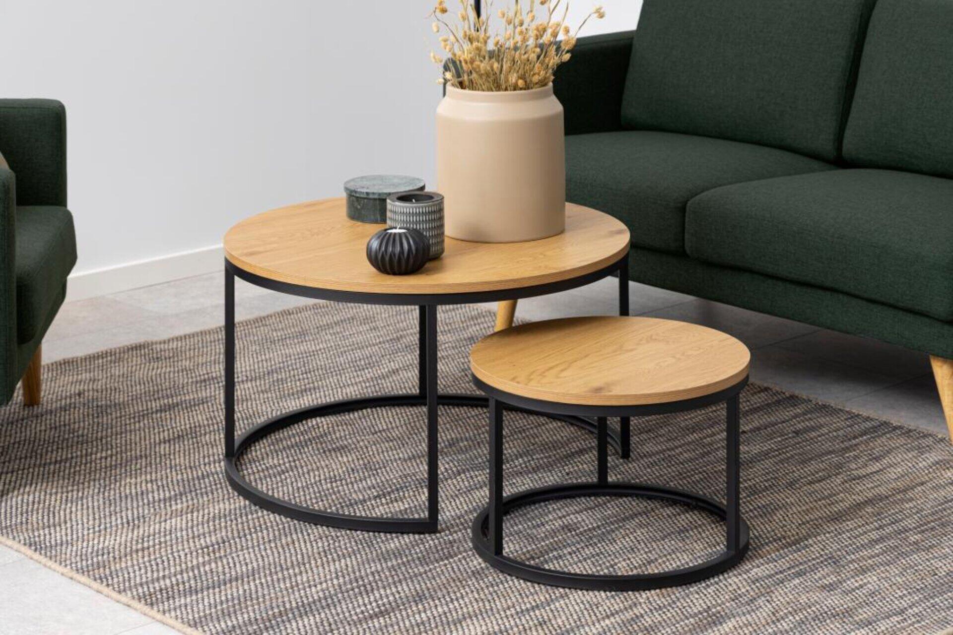 Couchtisch Spiro: Zwei runde Nesttische mit heller Holzplatte und schwarzem Metallgestell, dekorativ bestückt und in einem Wohnzimmerambiente platziert.