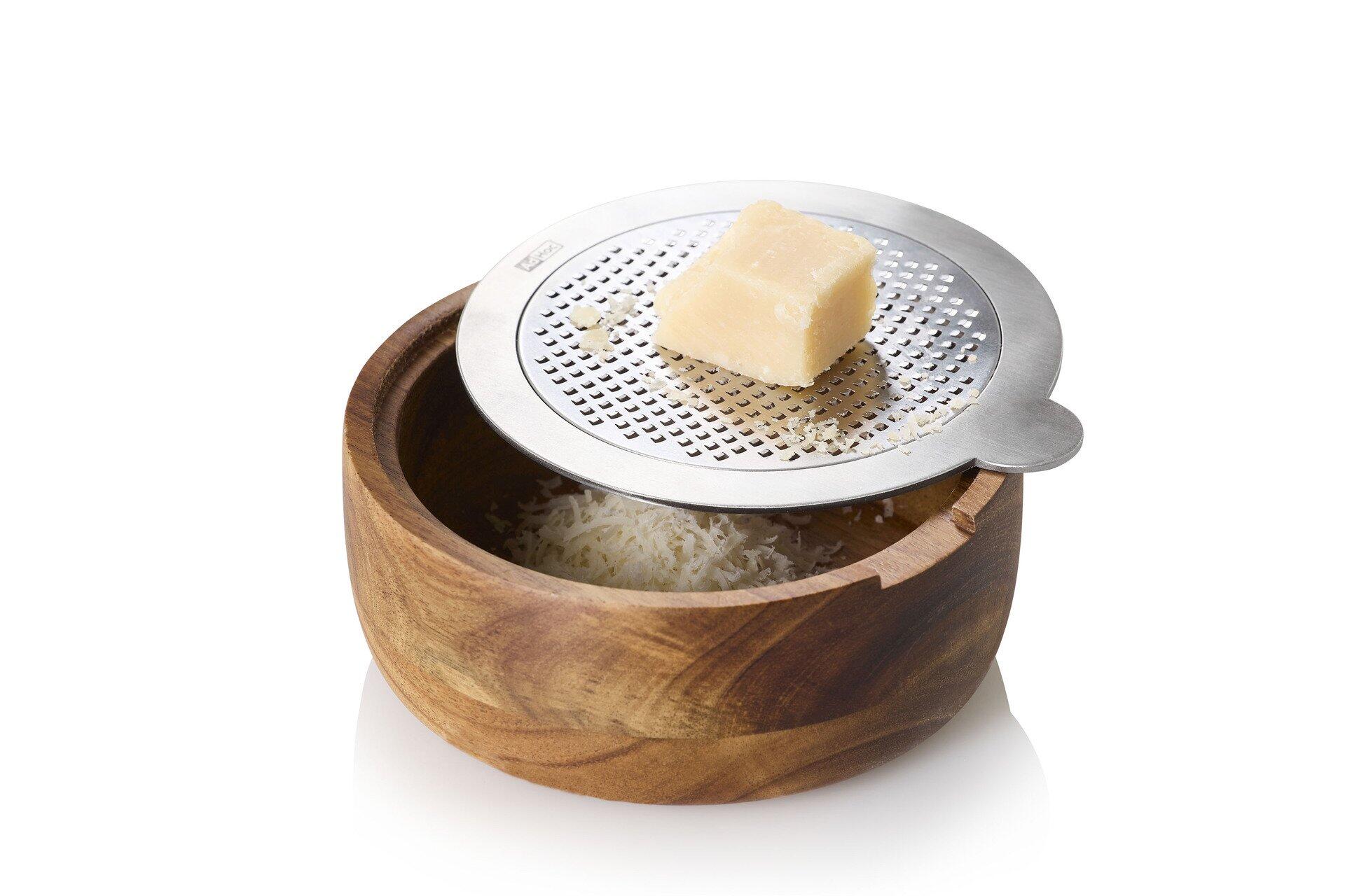 Nahaufnahme der Tisch-Feinreibe CutnServe mit Auffangbehälter aus dunklem Holz und Edelstahl-Käsehobel, der Käse reibt.