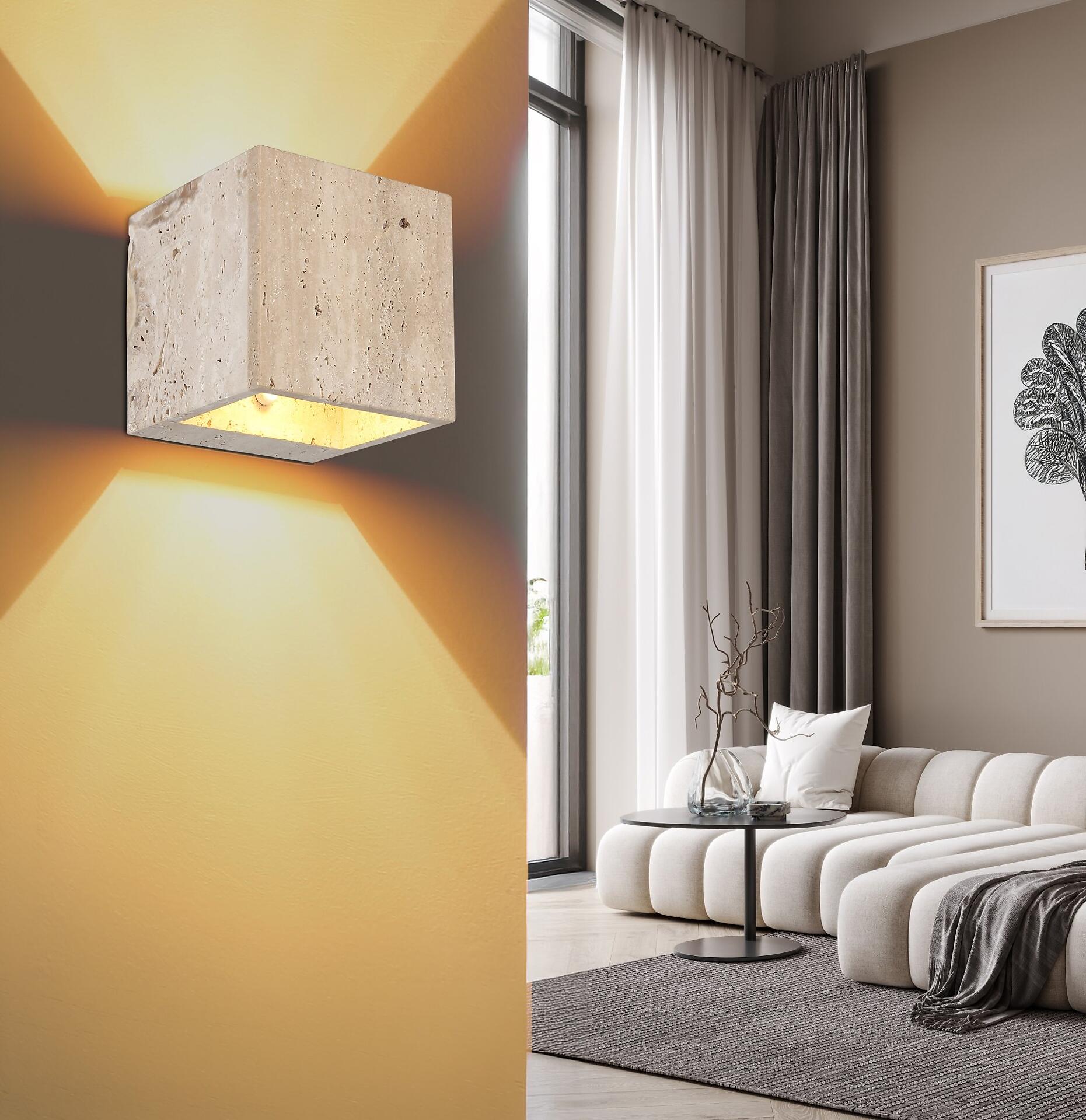 Wandleuchte ROJAS mit quadratischem Design aus Travertinstein, die warmes Licht an einer hellgelben Wand wirft und einen goldenen Schein erzeugt.