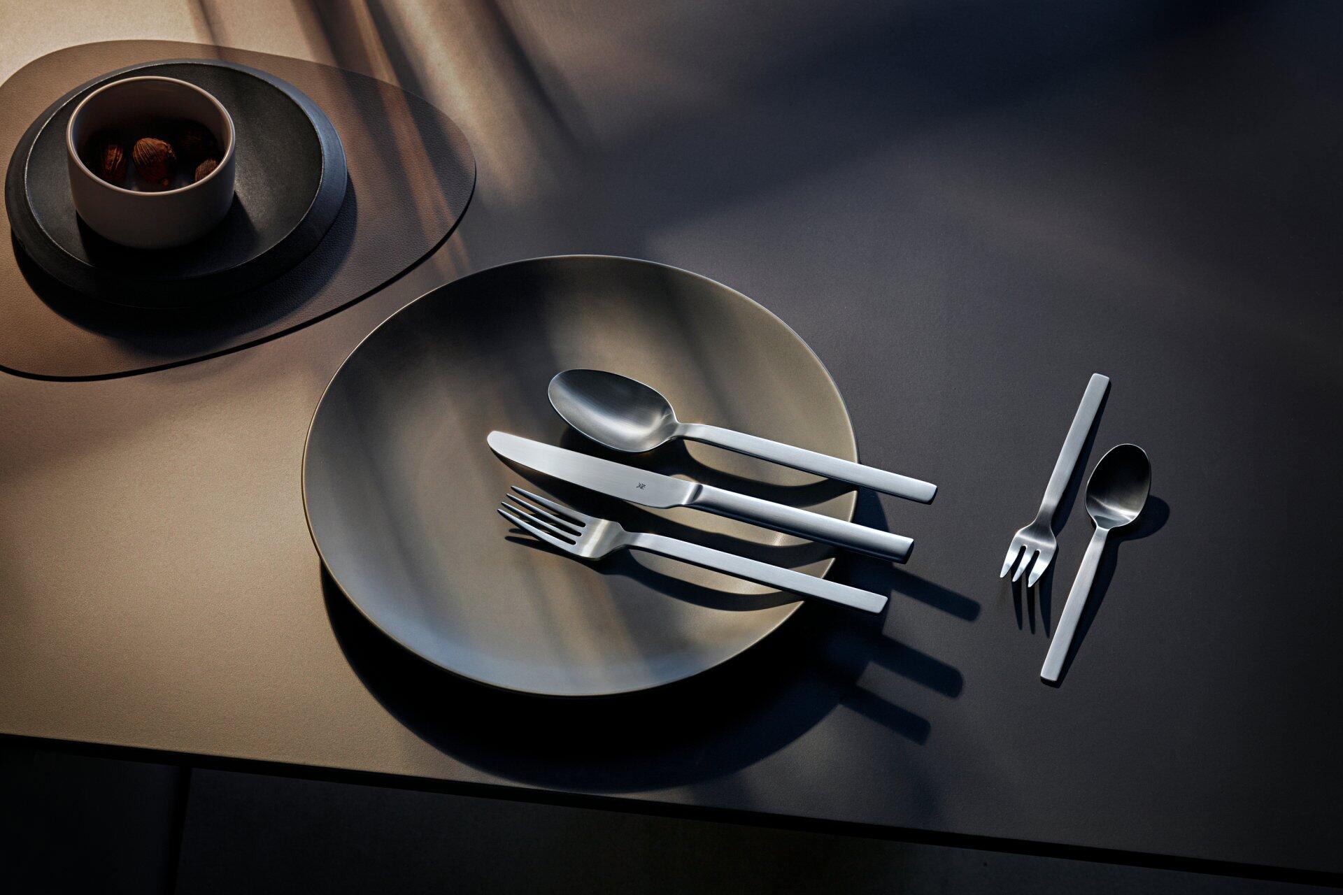 WMF Kaffeelöffel Alteo: stilvolles Besteck in diagonalem Arrangement auf dunkler Oberfläche, im Fokus das moderne Design und der silbern glänzende Look.