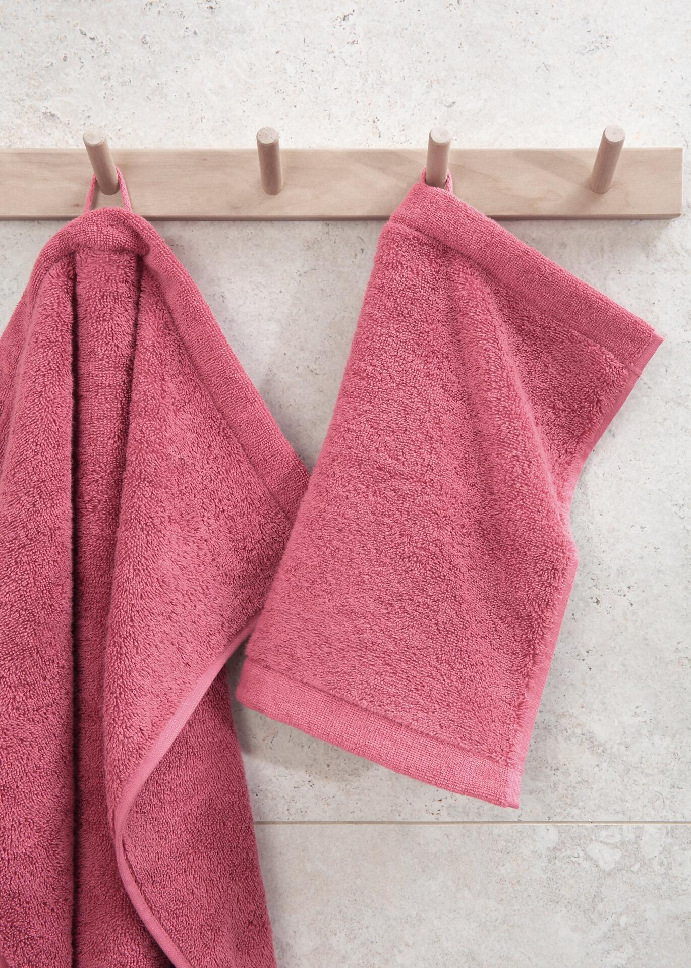 Rosa Waschhandschuh der Marke CAWÖ mit gerippter Textur, hängend an einem Holzhaken.