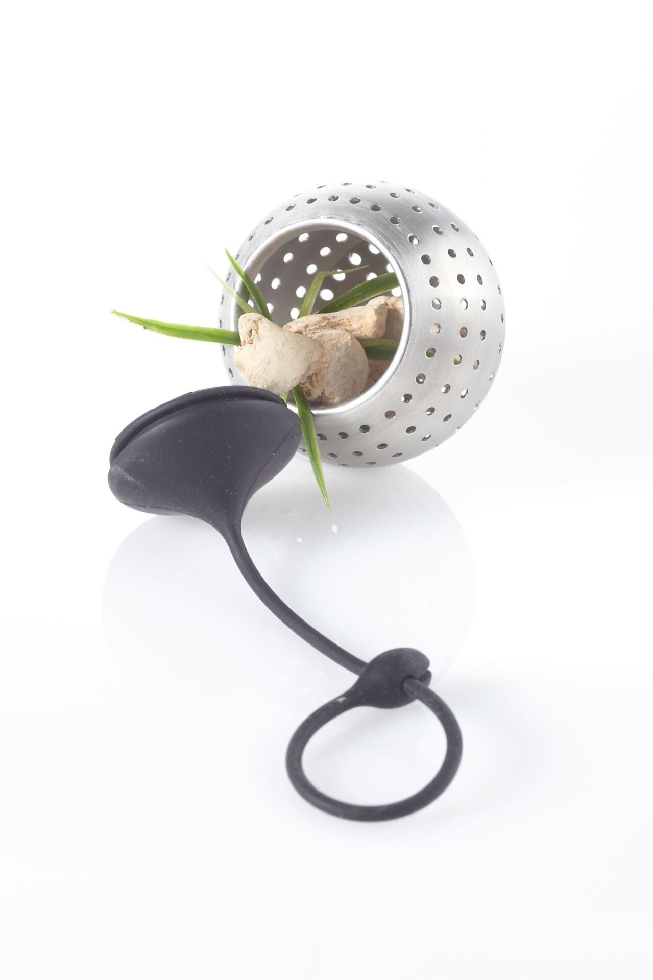 Gewürzfilter "Spice Bomb" aus Edelstahl mit Aufhänger, gefüllt mit Ingwer und Kräutern, dargestellt aus einer leicht unteren Perspektive, die die kugelförmige Form und die kleinen Löcher hervorhebt.
