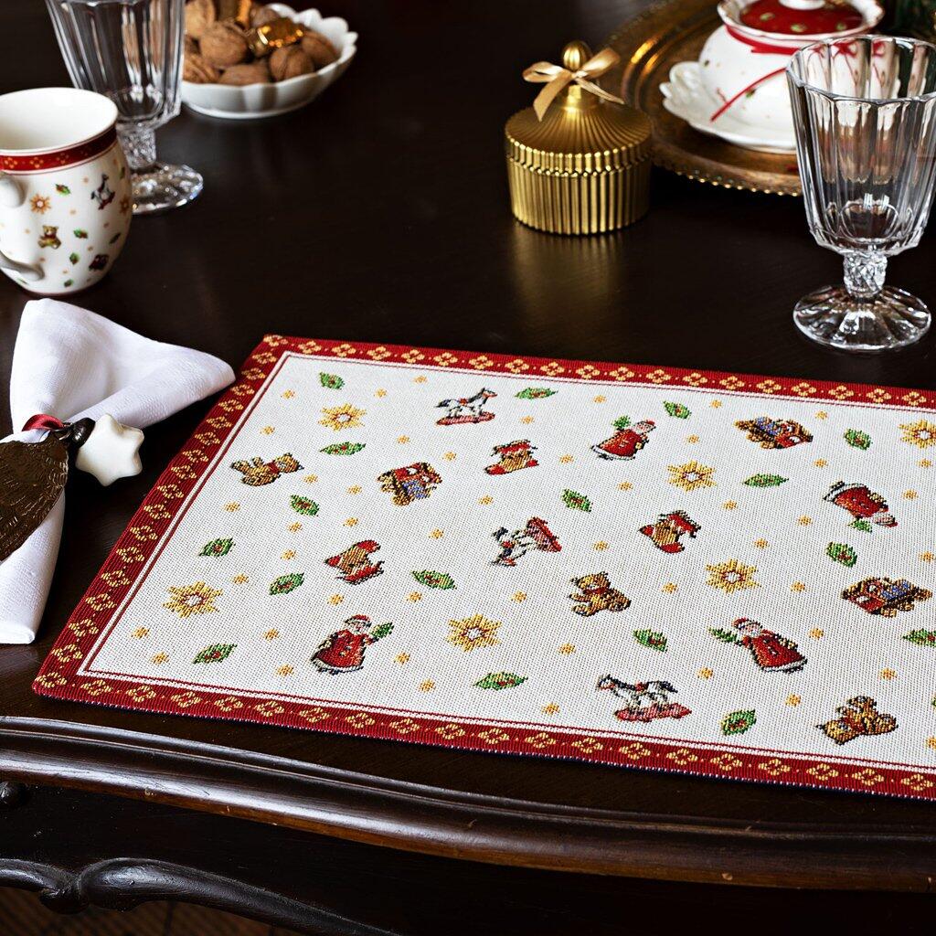 Weihnachtlich gestaltetes Gobelin Platzset Toy's Delight mit applizierten Weihnachtsmotiven wie Weihnachtsmännern, Glocken und Sternen auf cremefarbener Basis mit dunkelrotem Rand.