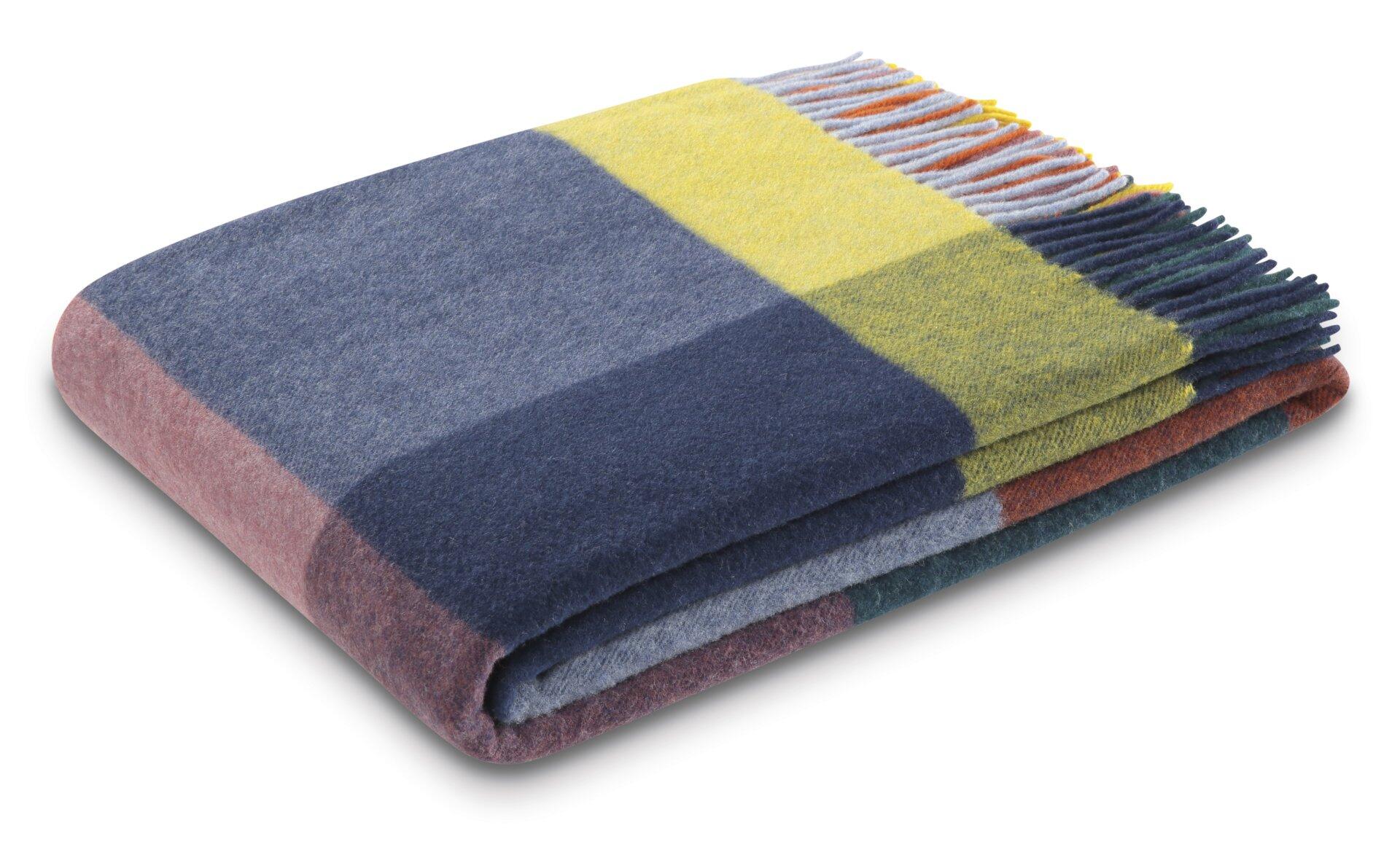 Plaid Decke mit karogestreiftem Muster in Blau, Rot, Gelb und Grün, gefaltet im 45-Grad-Winkel vor weißem Hintergrund, mit fransigen Kanten.