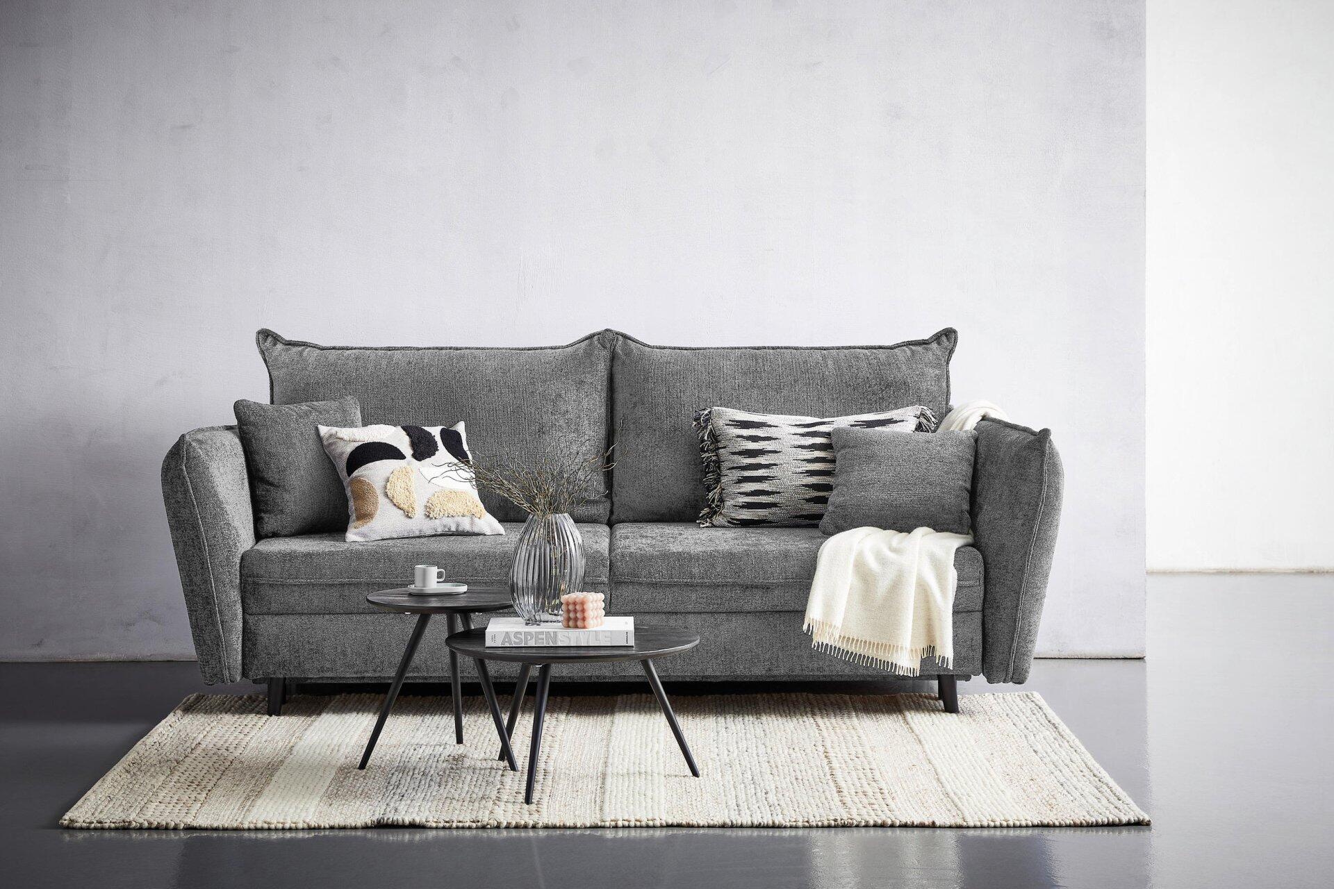 Frontalansicht des grauen Sofas Santana mit breiten Armlehnen, mehreren Rückenkissen und drei dekorativen Zierkissen auf einer erhöhten Perspektive.