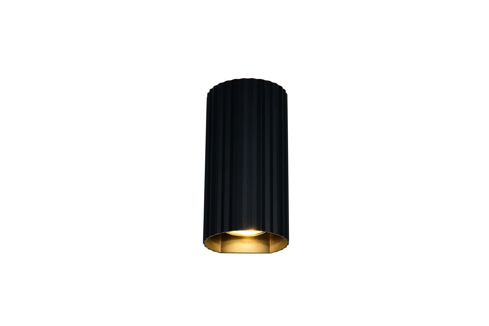 Schwarze, zylindrische Wandleuchte Soka mit vertikaler Rillenstruktur und goldfarbenem Reflektor, die in einer Frontalperspektive das nach unten gerichtete Licht zeigt.