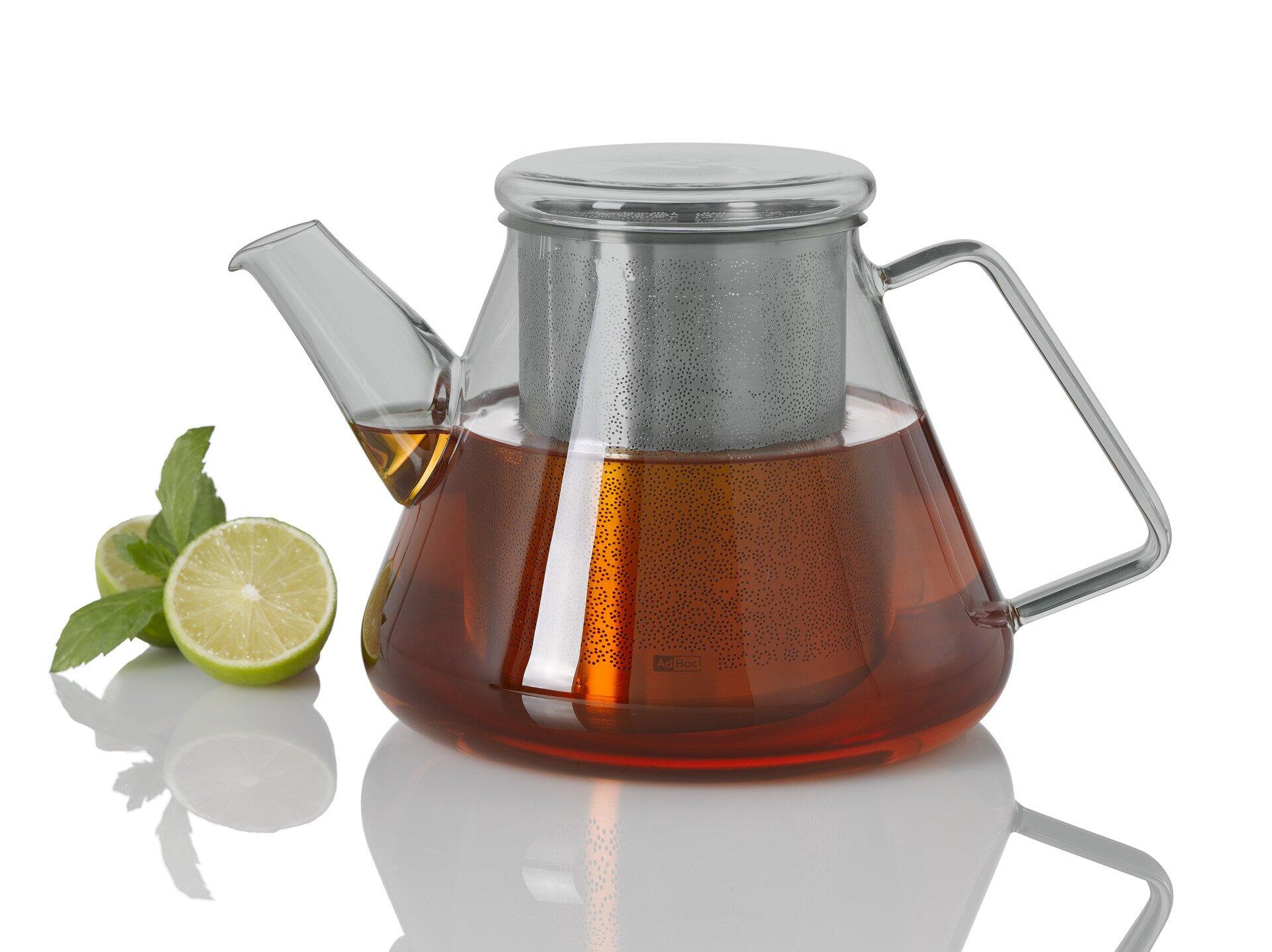 Teekanne Orient+ aus transparentem Glas mit gebogenem Ausgießer, Edelstahlgriff und integriertem Teesieb für lose Blätter, gefüllt mit dunklem Tee und stilvoll mit Limetten und Minze präsentiert.