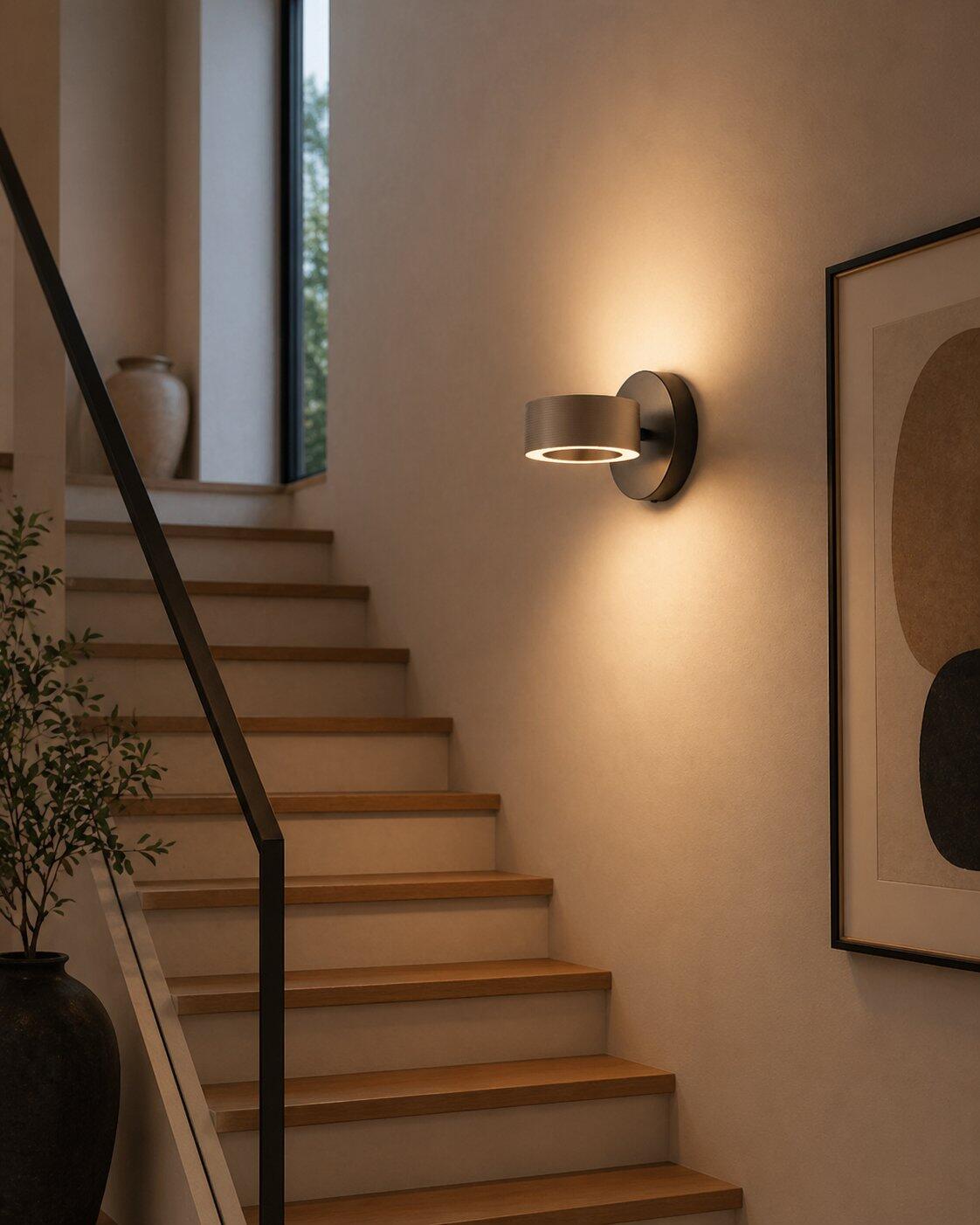 Wandleuchte Axion mit schwenkbarem Lampenkopf, befestigt an einer Treppe, zeigt die dimmbare Funktion mit warmem Licht.