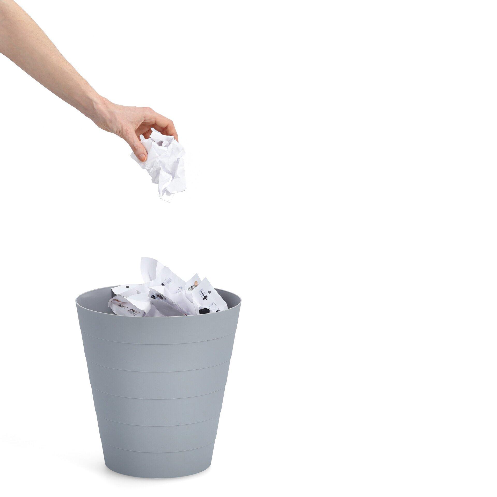 Grauer, zylindrischer Abfalleimer mit leicht erhöhtem Blickwinkel, zeigt eine Hand, die Papier in den gefüllten Mülleimer wirft.