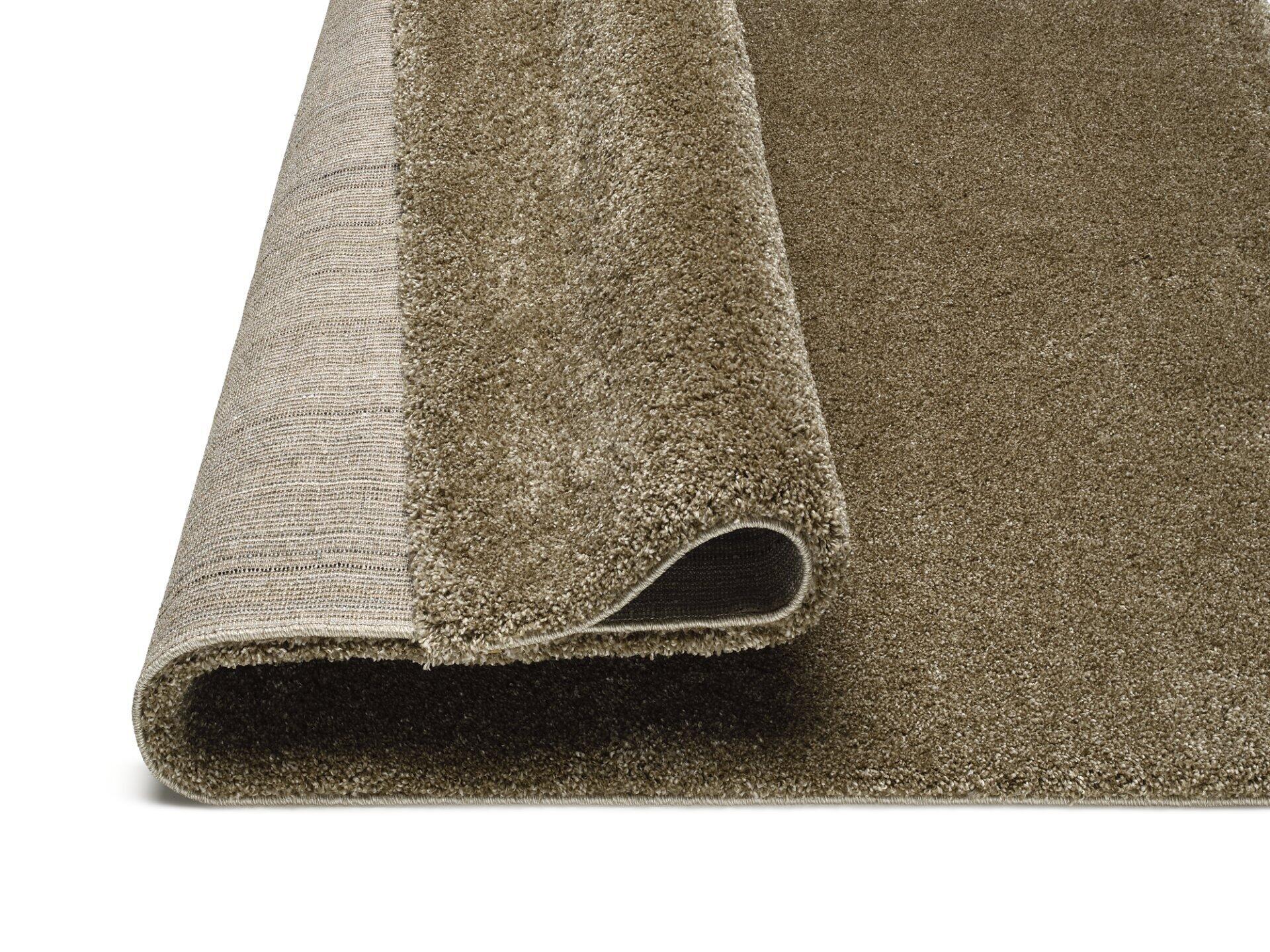 Gefalteter Maschinenwebteppich Erdara in graubrauner Hochflor-Optik mit sichtbarer hellbeige Unterseite und abgerundetem Etikett.
