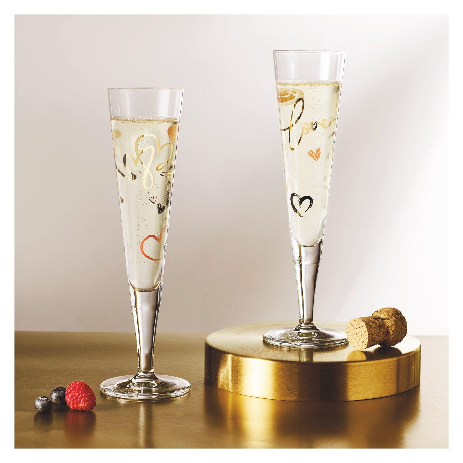 Zwei Champagnergläser mit goldenen Herzen und Sternen auf einem goldenen Podest, gefüllt mit Luftbläschen, präsentiert mit Früchten als festliche Dekoration.