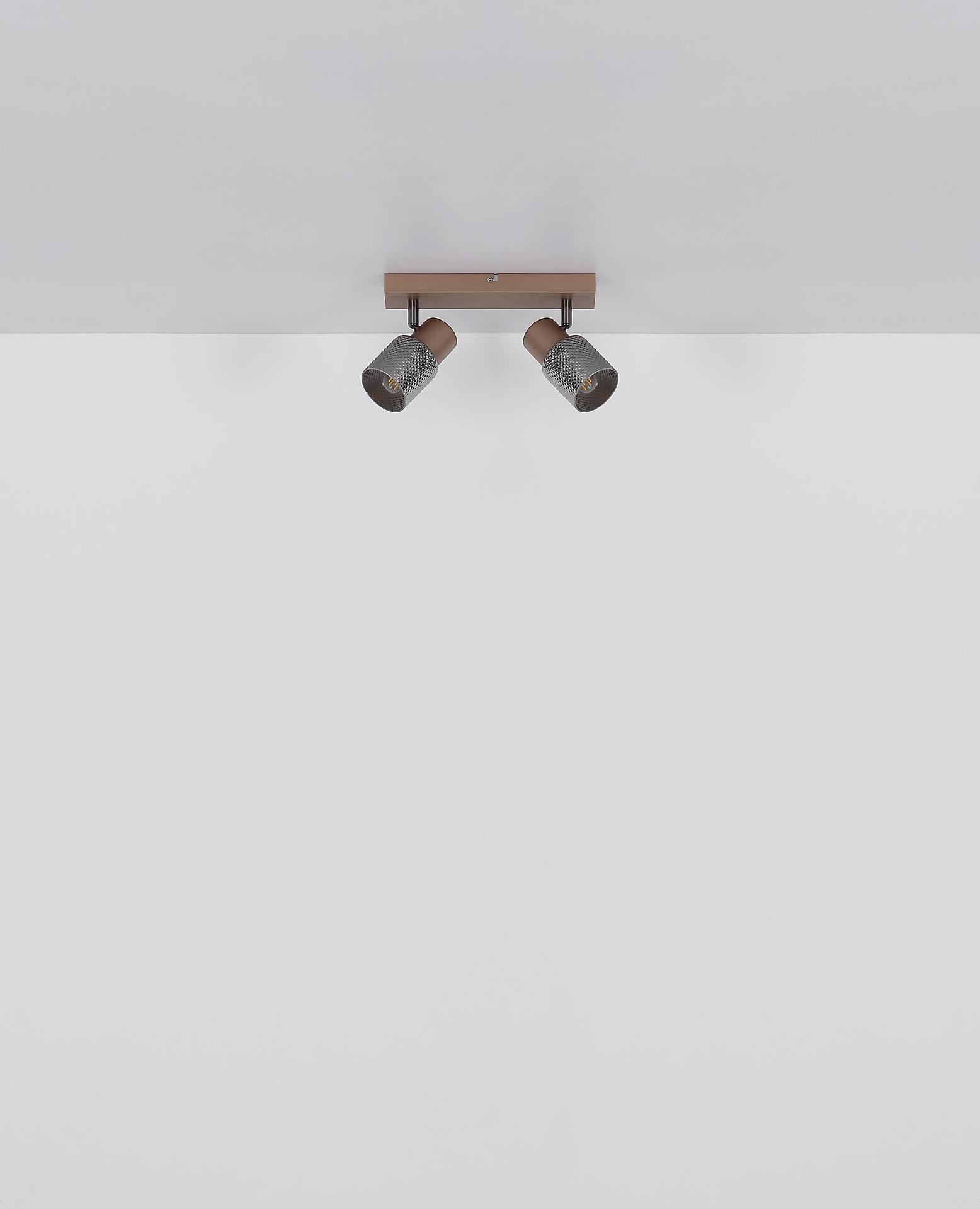 Wandlampe SATELLA mit Kupferoptik, zwei nach unten geneigten Armen und warmem Licht, frontal und leicht unterhalb aufgenommen.
