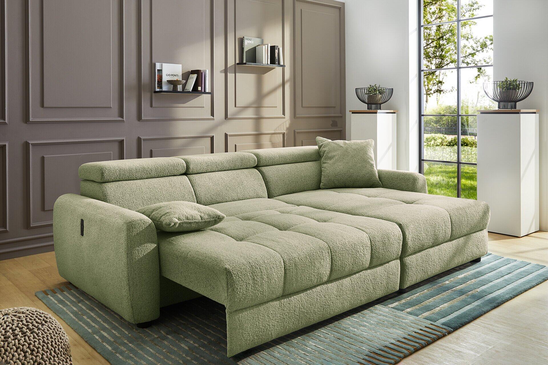 Helles Wohnsofa Move in blassgrün mit ausgeklappter Schlaffunktion und dekorativem Kissen, aus einer leicht erhöhten Frontalperspektive.