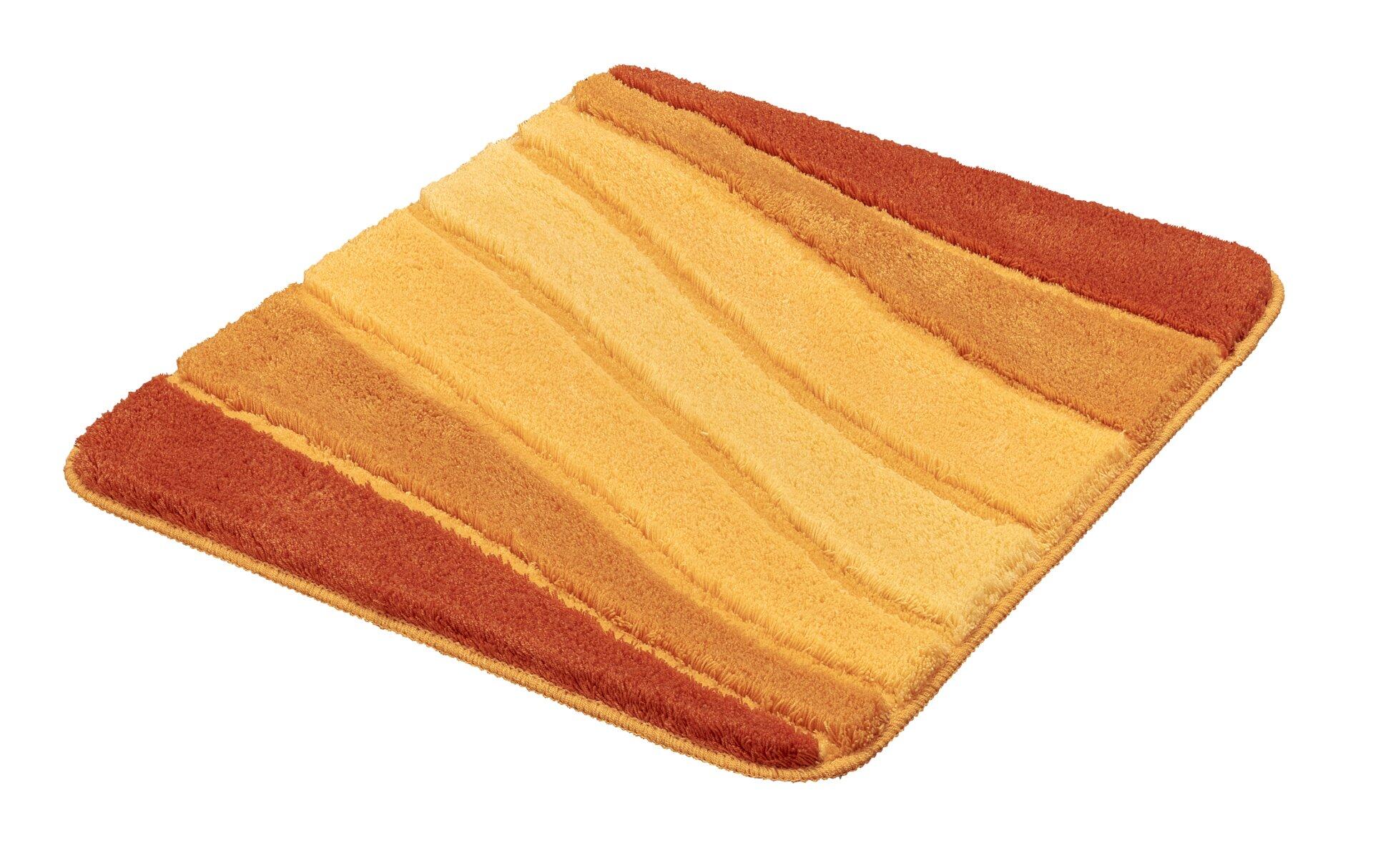 Badteppich Ocean mit geometrischem Streifenmuster in Beige, Gelb und Orange, leicht schräg auf weißem Hintergrund abgebildet.