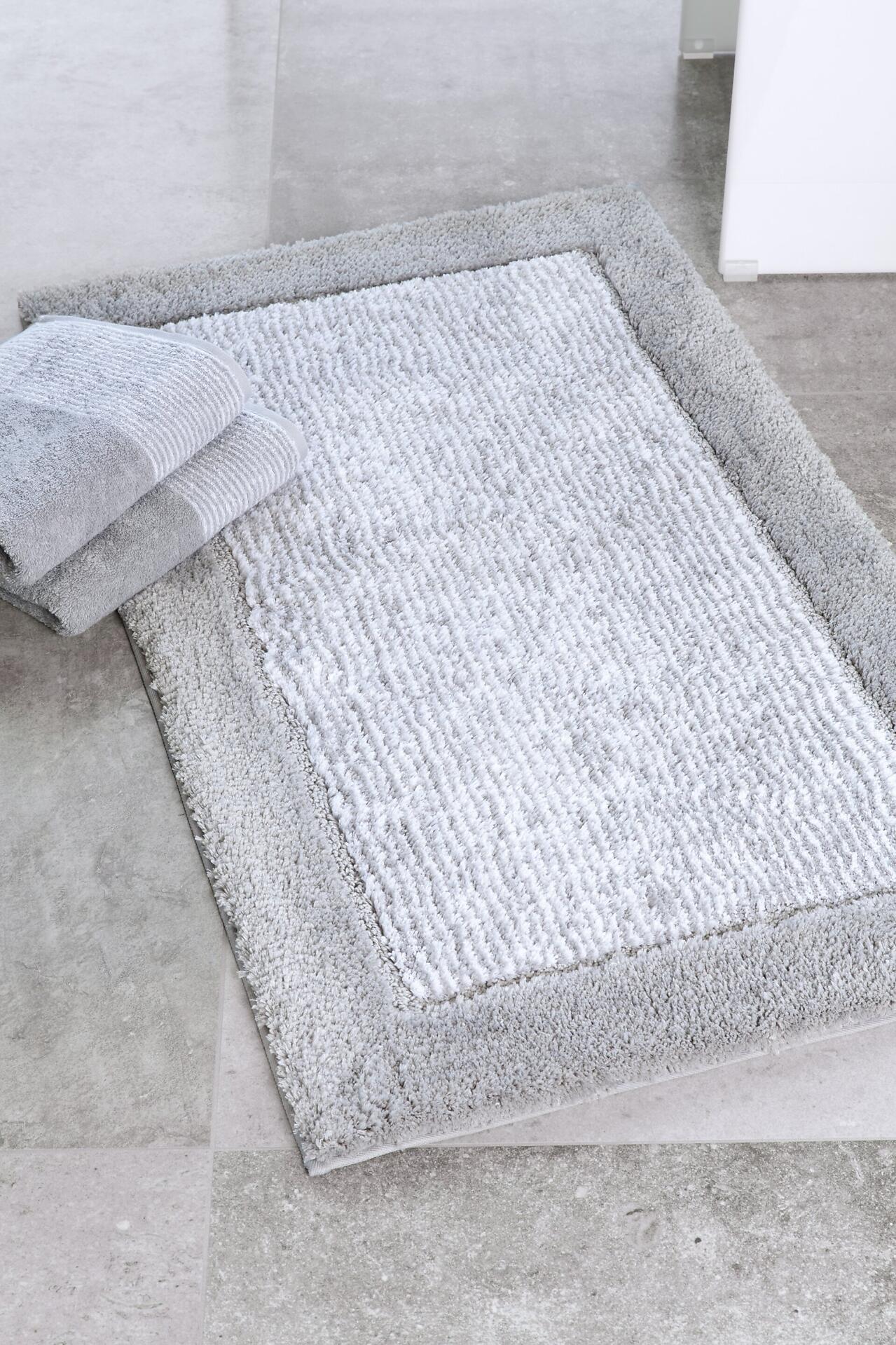 Zusammengefaltetes graues CAWÖ Two-Tone Handtuch auf einem flauschigen, strukturierten grauen Teppich.