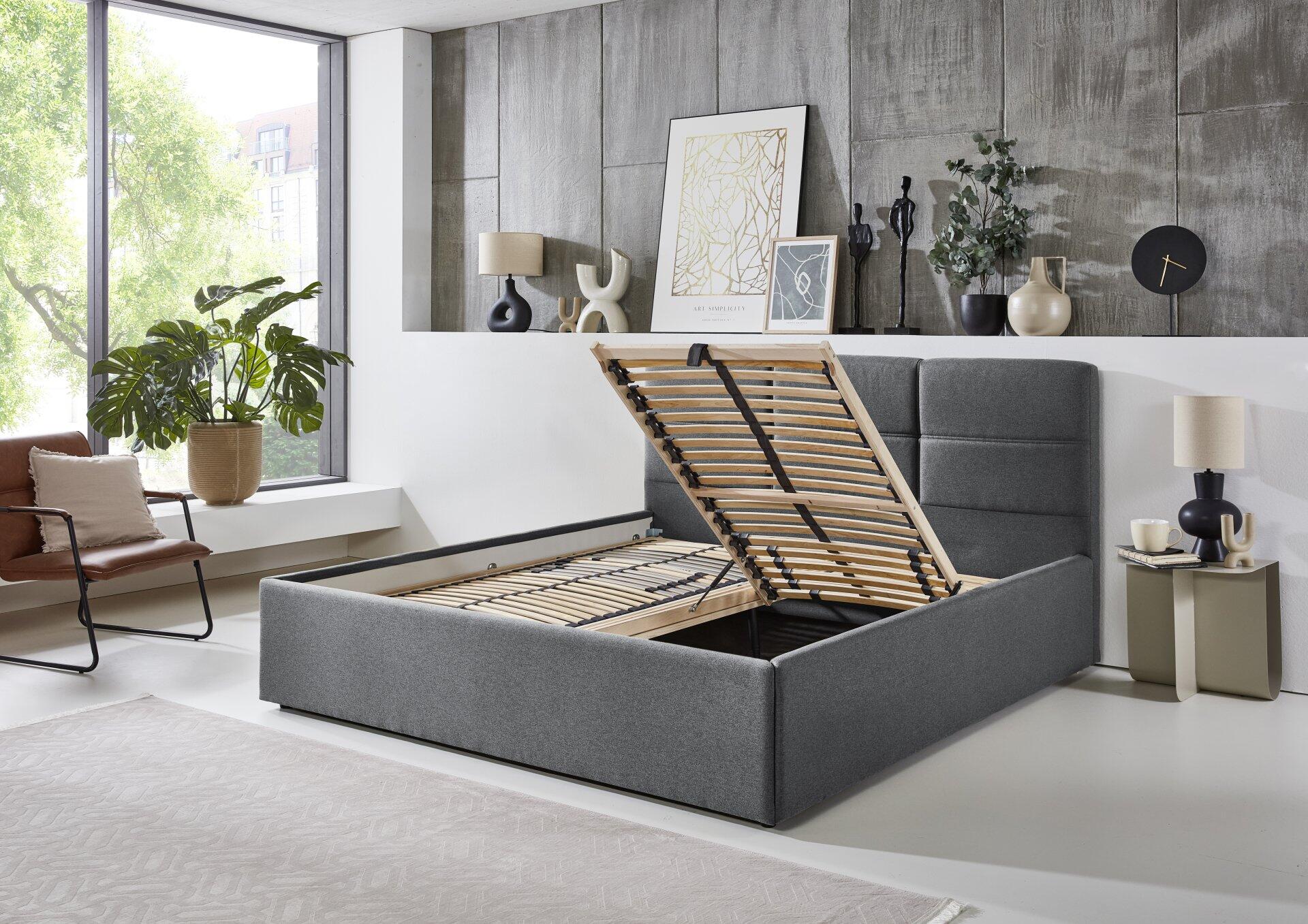 Polsterbett Durango PB100 mit grauem Stoffbezug und hochklappbarem Lattenrost, der Stauraum freigibt – Detailansicht in einer Innenansicht.