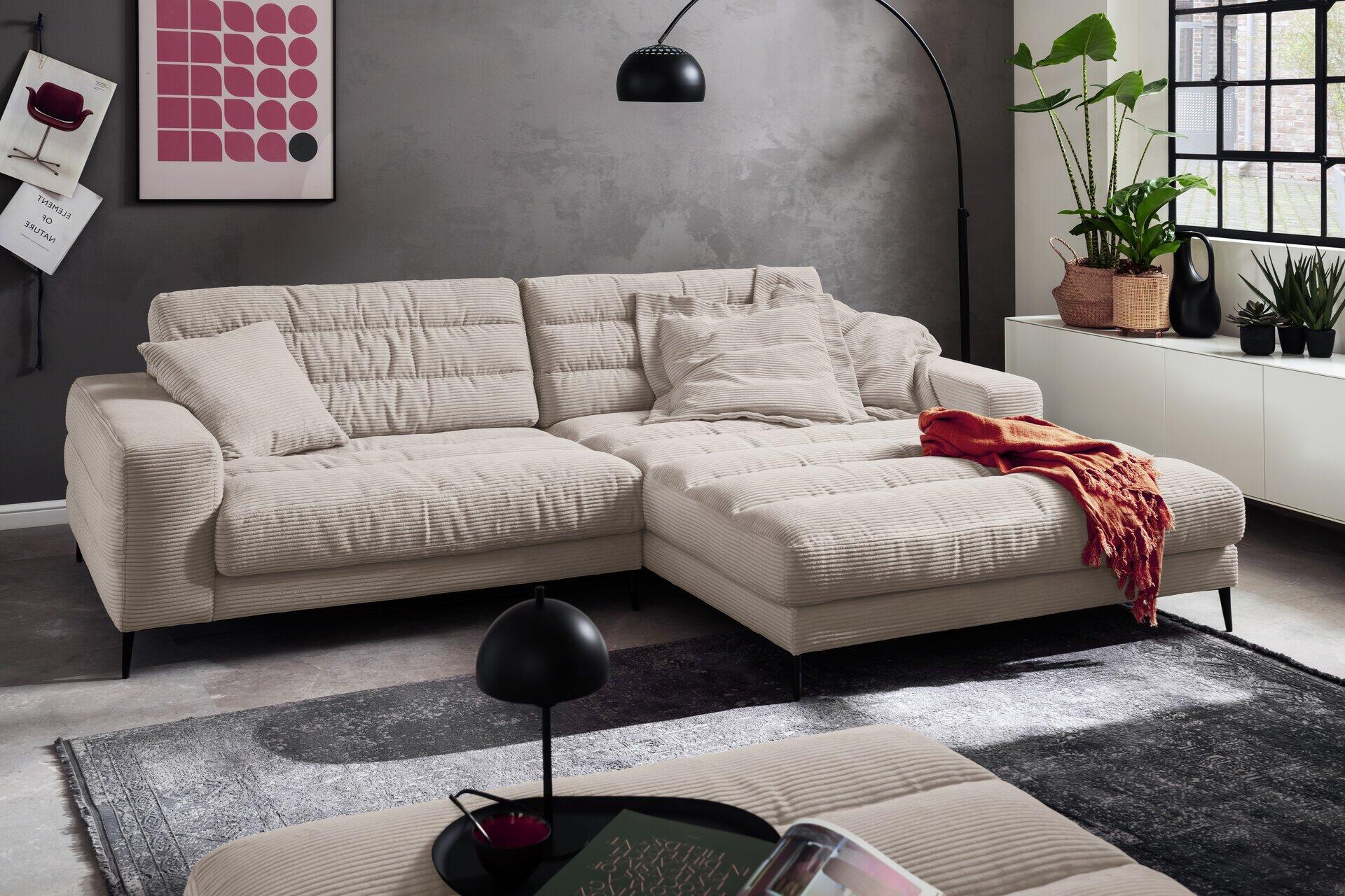 Polstergarnitur Badia, cremefarbenes Ecksofa mit schwarzem Metallfuß und sichtbarer Rippenstruktur, in einer modernen Wohnzimmerumgebung aus leicht erhöhter Perspektive.